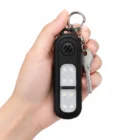 Czarny brelok-alarm z kółkiem na klucz trzymany w dłoni, białe tło
